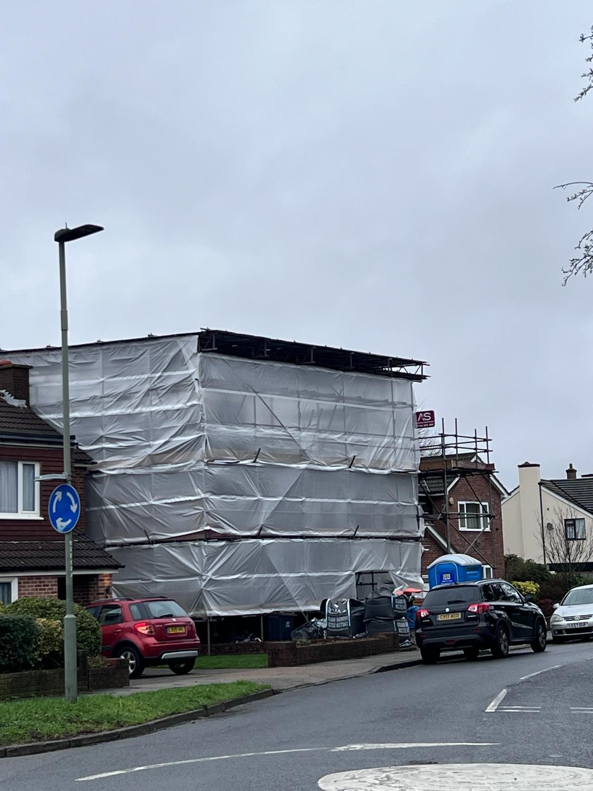 Temporary Roof Scaffolding - Armstrong Scaffolding Residential property with temporary roof scaffolding and white protective sheeting by Armstrong Scaffolding on a suburban street under a grey, overcast sky.