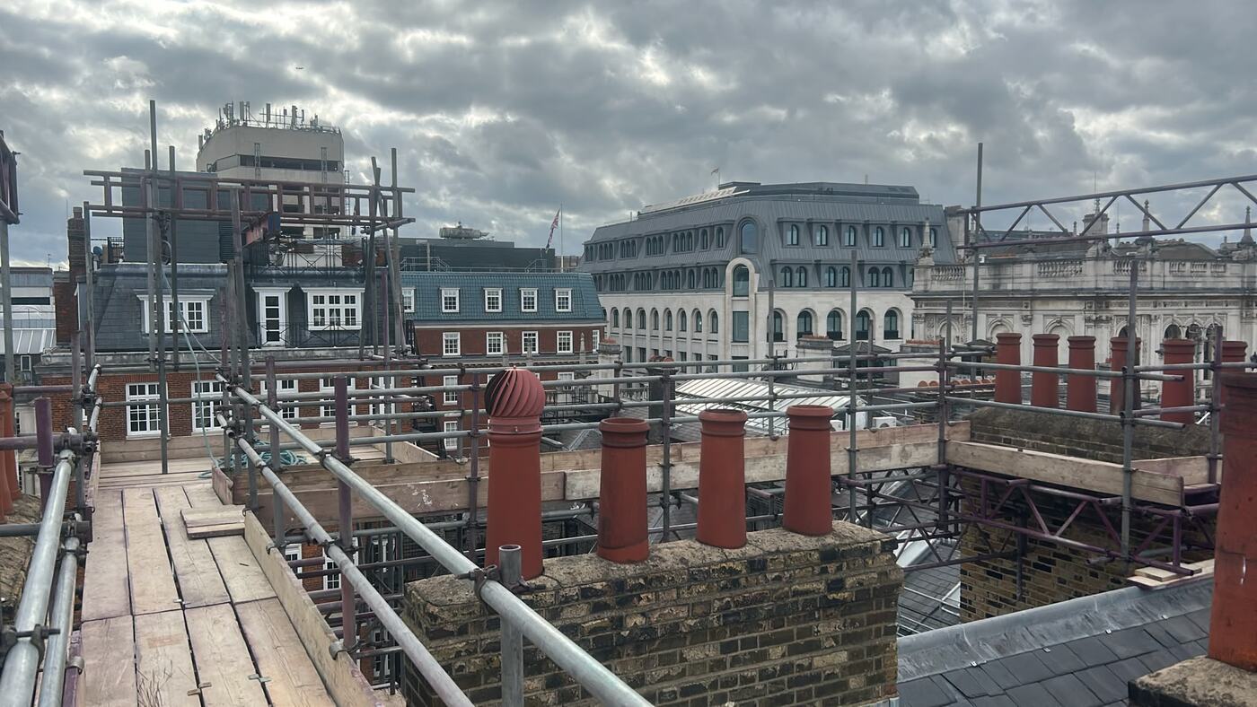 Chimney Stack Access for Flue Lining, Piccadilly - Armstrong Scaffolding Chimney stack scaffolding in Piccadilly London, boarded walkway and guardrails at roof level between brick stacks with red clay pots